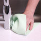 A green waffle weave towel being used by hand to clean a kitchen surface